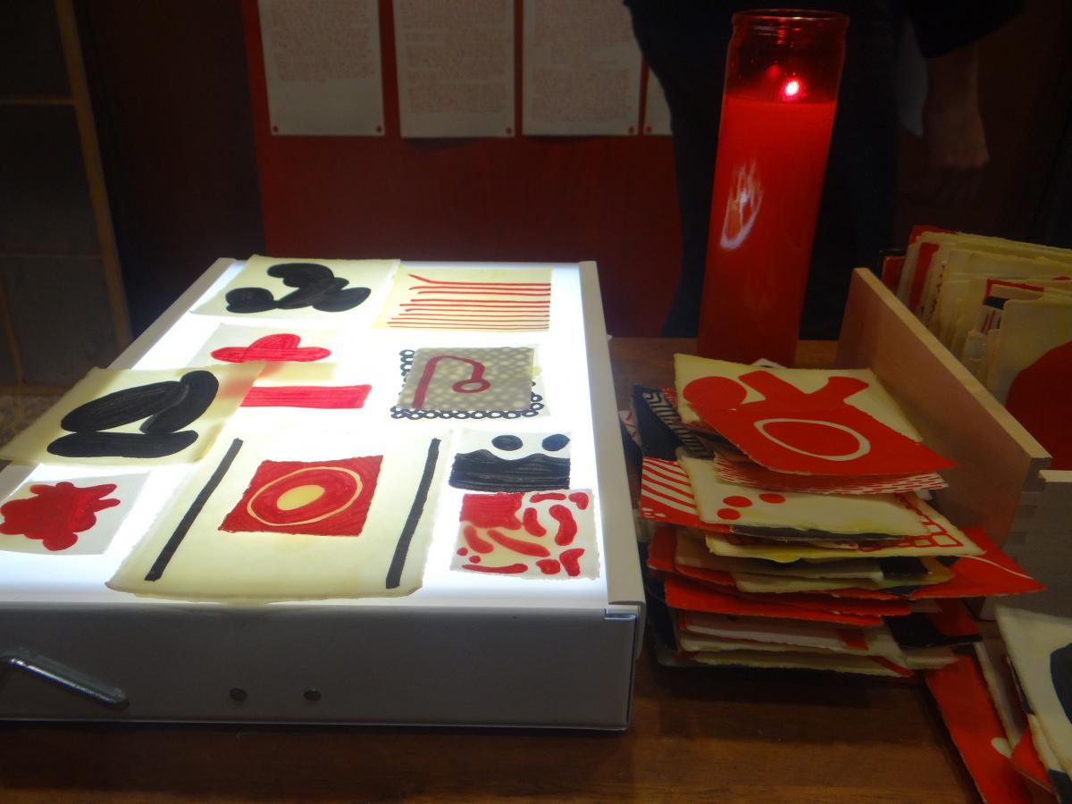 Josh T. France, In Tlilli, In Tlapalli: Three Tejanos in Red and Black (detail: Tejano/a Story-telling Table), 2013,  dinner tray, die-cut letters, beeswax-coated glyphs, light table, candle. Mulberry House, San Antonio. photo: Maya Cueva